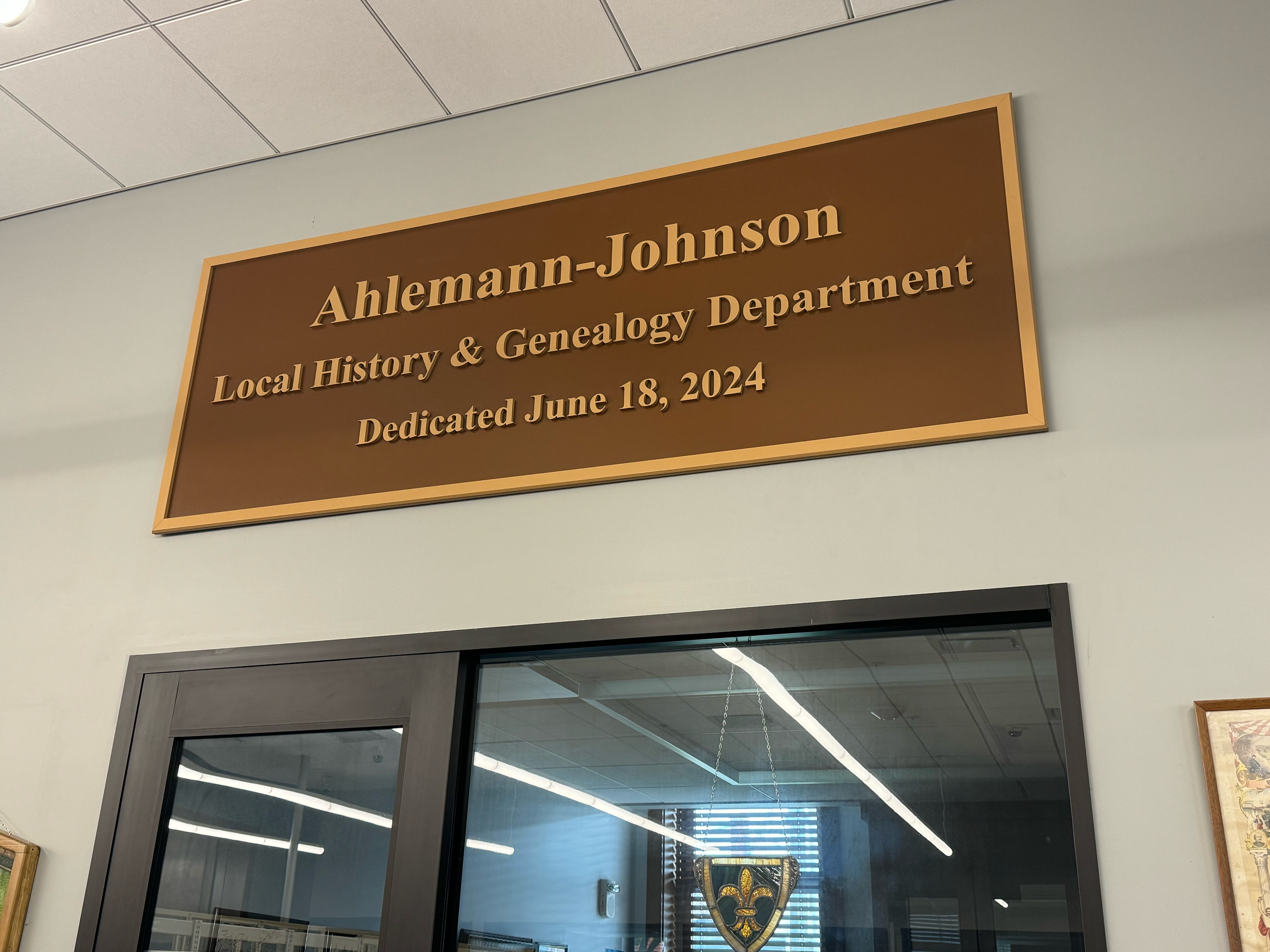 Wooden plaque reading Ahlemann-Johnson Local History & Genealogy Department Dedicated June 18, 2024