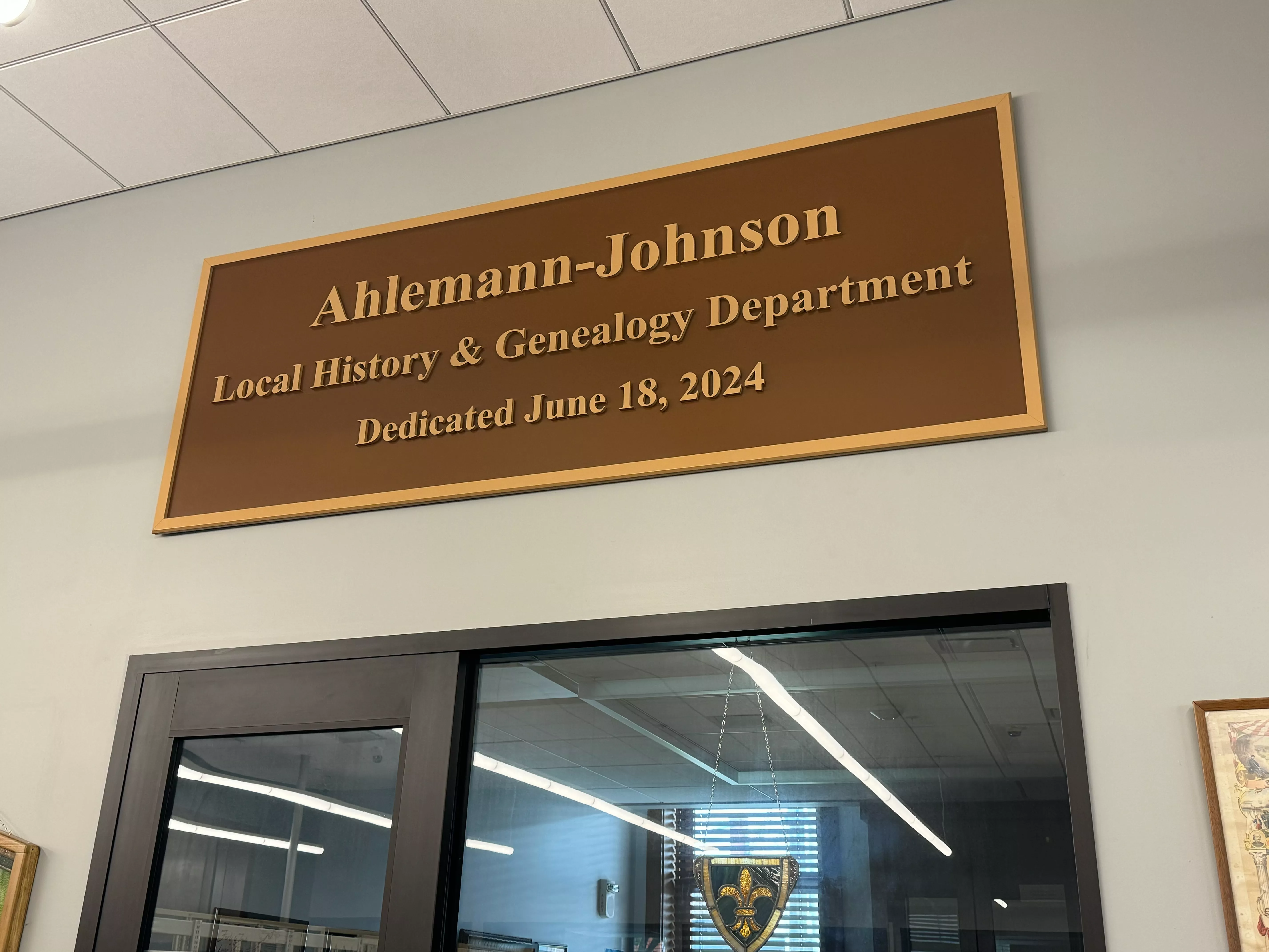 Wooden plaque reading Ahlemann-Johnson Local History &amp; Genealogy Department Dedicated June 18, 2024